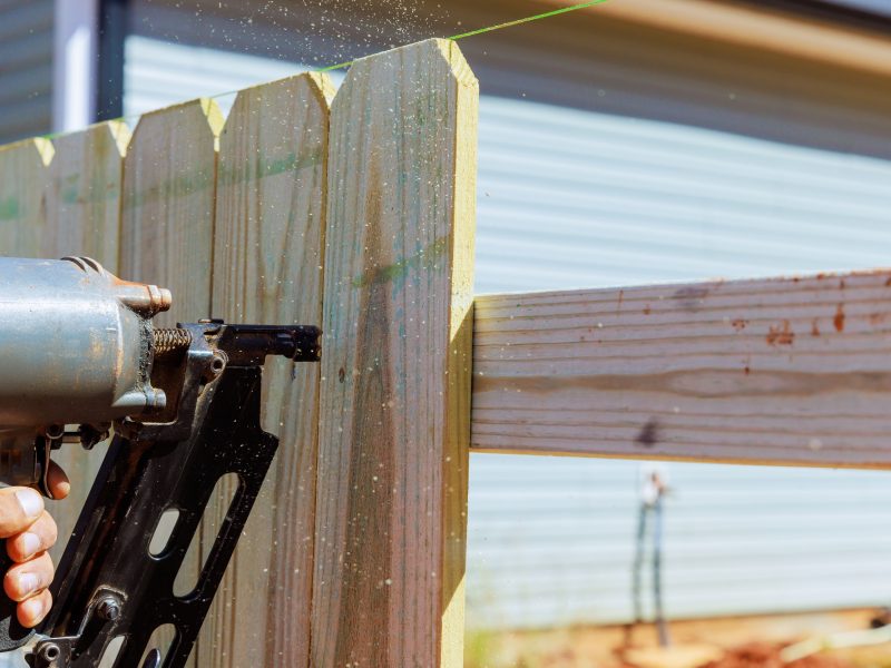 Worker uses an air pneumatic gun to nail wooden planks to a fence during work Worker uses an air pneumatic gun to nail wooden planks to a fence during work